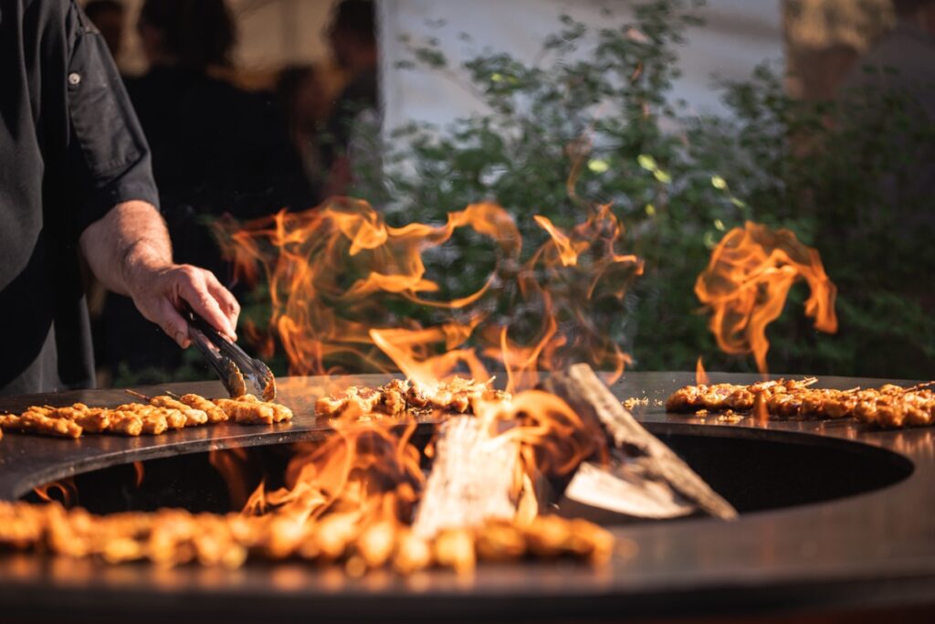 Chef grilt vleesbrochettes op Ofyr barbecue met zichtbare vlammen